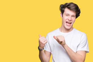 Yakışıklı delikanlı üzerinde rahat beyaz t-shirt giyen izole arka plan emin gülümseyen arkasından el ve kadar başparmak ile işaret