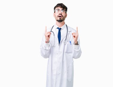 Giyen hastane kat izole arka plan üzerinden hayran ve yukarıya bakıyor ve parmakları ile işaret ve silah kaldırdı sürpriz bir adam genç doktor.