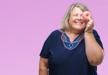 Kıdemli artı boyutu üzerinde şeker donut yemek kafkas kadın arka plan ayakta ve diş gösterilen kendine güvenen bir gülümsemeyle gülümseyerek mutlu bir yüz ile izole