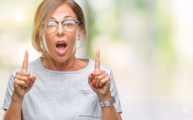 İzole arka plan üzerinde gözlük takan orta yaş İspanyol kadın kıdemli hayran ve yukarıya bakıyor ve parmakları ile işaret ve silah kaldırdı şaşırttı.