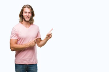 Gülümseyen ve iki elleri ve parmakları ile tarafına işaret kamera bakarak izole arka plan üzerinde uzun saçlı yakışıklı delikanlı.