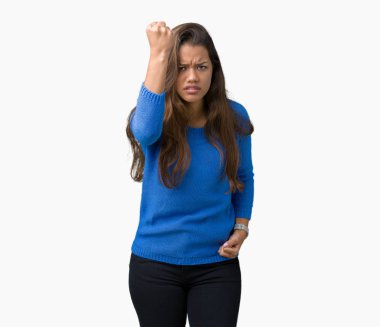 Öfkeli ve sinirli sinirli ve öfke ile bağırarak süre öfkeli yumruk yükselterek izole arka plan üzerinde mavi kazak giyen genç güzel esmer kadın. Öfke ve agresif kavramı.