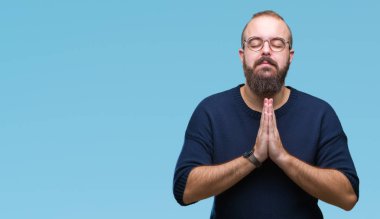 Genç beyaz hipster adam eliyle birlikte AF emin gülümseyen için soran dua izole arka plan üzerinde güneş gözlüğü takıyor.