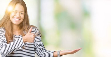 Giyen genç güzel esmer kadın kazak izole arka plan gösteren palm el ve iş tamam jestle üzerinde başparmak yukarı, gülümseyen mutlu ve neşeli çizgili.