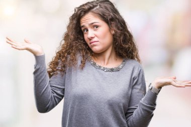 Güzel esmer kıvırcık saçlı Genç kız izole arka plan clueless ve şaşkın bir ifadeyle kollar ve eller kaldırdı üzerinde bir kazak giyiyor. Şüphe kavramı.