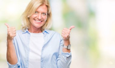 Orta yaş sarışın kadın el ile pozitif jest yapıyor izole arka plan başarı işareti yüzünden başparmak gülümseyen ve mutlu. Neşeli bir ifadeyle, kazanan jest kameraya bakıyor.