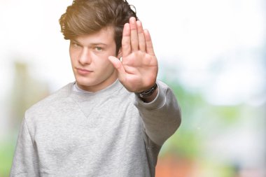 Young handsome sporty man wearing sweatshirt over isolated background doing stop sing with palm of the hand. Warning expression with negative and serious gesture on the face. clipart