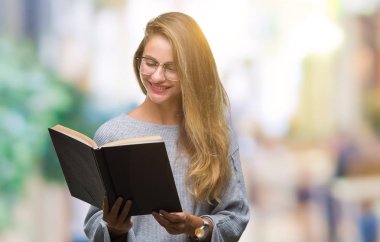 Genç güzel sarışın kadın ayakta ve diş gösterilen kendine güvenen bir gülümsemeyle gülümseyerek mutlu bir yüz ile izole arka plan üzerinde bir kitap okuma