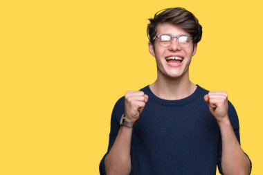 Yakışıklı delikanlı izole arka plan üzerinde kutluyor gözlük takan şaşırttı ve başarı için kaldırdı kollarını açarak hayret ve gözleri açık. Kazanan kavramı.