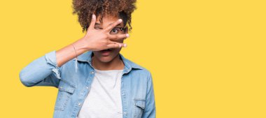 Mahcup ifadeyle parmaklarımın arasından yüz ve gözler el ile kapsayan şok bakmak izole arka plan üzerinde gözlük güzel genç Afro-Amerikan kadın arıyor.