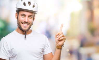 Kameraya bakarak yan el ve parmak ile işaret eden genç yakışıklı adamın yüzünde kocaman bir gülümseme ile izole arka plan üzerinde bisikletçi Güvenlik kask giydiğini.