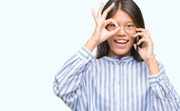 年轻的亚洲妇女在电话结束在孤立的背景与愉快的面孔微笑做 标志用手在眼睛看通过手指 — 图库照片