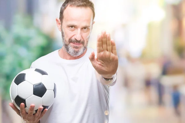 中年白发老人拿着足球在孤立的背景上 张开手做停止标志 用严肃而自信的表情 防守姿态 — 图库照片