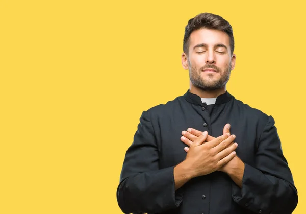 目を閉じて胸に手と感謝のジェスチャーの顔に笑みを浮かべて隔離された背景に若いカトリックのキリスト教司祭男 健康の概念 — ストック写真