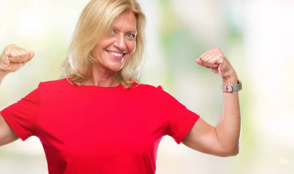 Middle age blonde woman over isolated background showing arms muscles smiling proud. Fitness concept.