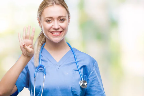 年轻的金发医生的妇女在孤立的背景显示和指向四的手指 而微笑着自信和快乐 — 图库照片