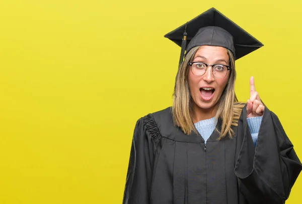Young beautiful woman wearing graduated uniform over isolated background pointing finger up with successful idea. Exited and happy. Number one.