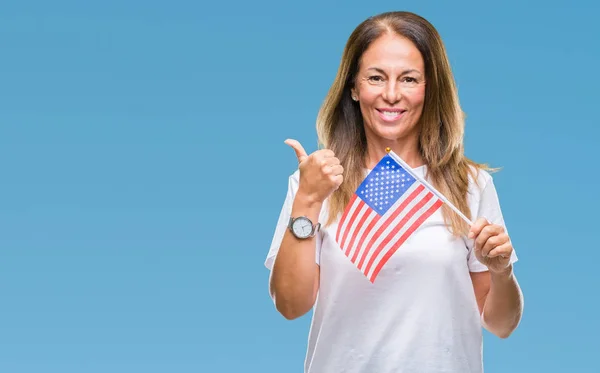 Middle age hispanic woman holding flag of United States of America over isolated background pointing and showing with thumb up to the side with happy face smiling