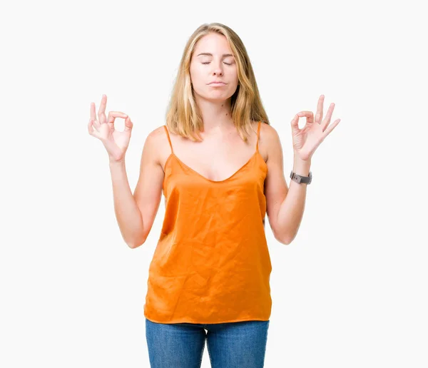 Beautiful young woman wearing orange shirt over isolated background relax and smiling with eyes closed doing meditation gesture with fingers. Yoga concept.