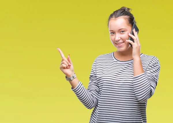 側の手と指で指す非常に幸せな孤立した背景にスマート フォンで話している若い美しい白人女性 — ストック写真