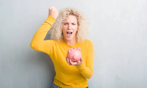 Joven Mujer Rubia Sobre Fondo Gris Grunge Sosteniendo Alcancía Molesto — Foto de Stock