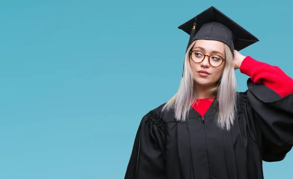 年轻的金发女子穿毕业制服在孤立的背景混淆和疑惑的问题 疑惑不定 用手在头上思考 沉思概念 — 图库照片