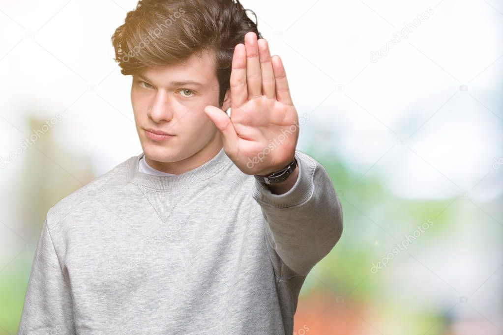 Young handsome sporty man wearing sweatshirt over isolated background doing stop sing with palm of the hand. Warning expression with negative and serious gesture on the face.