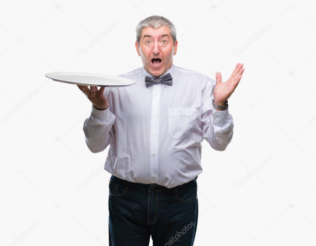 Handsome senior waiter man holding silver tray over isolated background very happy and excited, winner expression celebrating victory screaming with big smile and raised hands