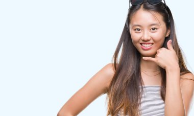 Genç Asyalı kadın yapıyor gülümseyen izole arka plan üzerinde güneş gözlüğü takıyor telefon hareketi ile el ve parmak telefonda konuşuyor gibi. Kavramları iletişim.