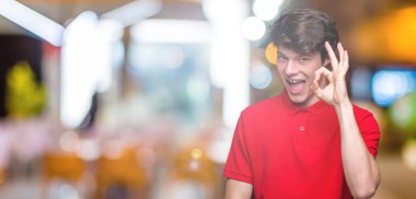 İzole arka plan el ve parmaklar ok işaretiyle yapıyor olumlu gülümseyen üzerinde kırmızı t-shirt giyen genç yakışıklı adam. Başarılı ifade.