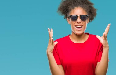 Genç afro Amerikalı kadın üzerinde güneş gözlüğü takıyor arka plan deli izole ve deli bağırarak ve agresif ifade ve silah kaldırdı bağırıyor. Hayal kırıklığı kavramı.