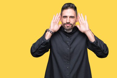 Genç Hıristiyan rahip kulak jest, dedikodu için meraklı her iki ellerde dinliyoruz izole arka plan üzerinde. İşitme sorunu, sağır