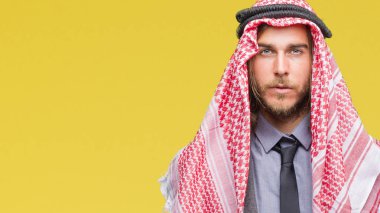 Genç yakışıklı Arap adam uzun saçlı yüzünde ciddi bir ifade ile izole arka plan üzerinde keffiyeh giyiyor. Basit ve doğal kameraya bakıyor.