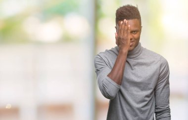 El yüz ve sürpriz duygu kendinden emin gülümseme ile tek gözüyle kapsayan izole arka plan üzerinde genç Afro-Amerikan adam.