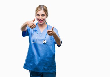 Genç güzel sarışın doktor cerrah hemşire kadın el ile pozitif jest yapıyor onaylama izole arka plan üzerinde başparmak gülümseyen ve başarı için mutlu. Kamera, kazanan jest arıyorsunuz.