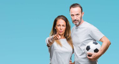 Orta yaş İspanyol çift futbol futbol topu tutan kamera ve size parmak ile işaret arka plan izole, el işareti, pozitif ve kendinden emin bir jest ön