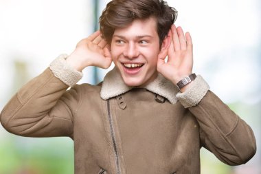 Her ikisi de dinliyoruz izole arka plan üzerinde kış ceket giyen genç yakışıklı adam kulak jest, dedikodu için meraklı eller. İşitme sorunu, sağır