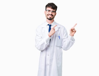 Gülümseyen ve iki elleri ve parmakları ile tarafına işaret kamera bakarak izole arka plan üzerinde beyaz önlük giyen genç profesyonel bilim adamı.