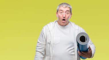 Üst düzey yakışıklı yoga mat izole arka plan üzerinde bir sürpriz yüz, korkuyor ve heyecanlı korku ifadesi ile şok korkmuş holding