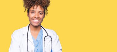 İzole arka plan mutlu yüz çapraz silah kameraya bakarak ile gülümseyen genç Afro-Amerikan doktor kadın. Olumlu bir kişi.