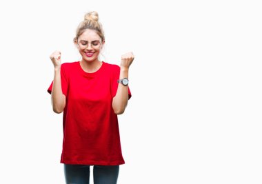 Kırmızı t-shirt ve gözlük izole arka kolları olan başarı için heyecan üzerinde giyen genç güzel sarışın kadın kutluyor zafer gülümseyen kaldırdı. Kazanan kavramı.