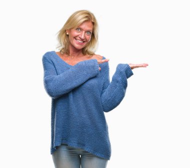 Hayret ve el ile sunulması ve parmak ile işaret ederken kameraya gülümseyen izole arka plan üzerinde kış kazak giyen orta yaş sarışın kadın.