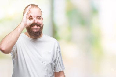 Gülümseyen, parmakları ile mutlu yüz üzerinden seyir göz el ile ok jest yapıyor izole arka plan üzerinde rahat t-shirt giyen genç beyaz hipster adam.