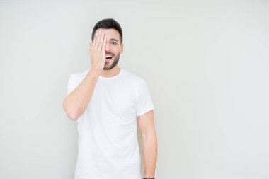 Üzerinde rahat beyaz t-shirt giyen genç yakışıklı adam arka plan kapsayan bir göz yüz ve sürpriz duygu kendinden emin gülümseme ile el ile izole.