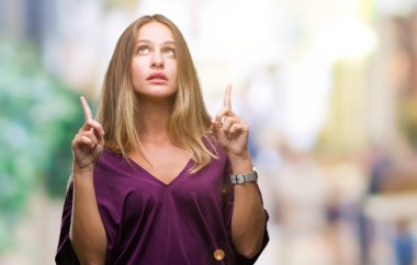 Genç güzel sarışın zarif kadın izole arka plan üzerinden hayran ve yukarıya bakıyor ve parmakları ile işaret ve silah kaldırdı şaşırttı.