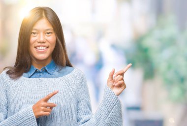 Gülümseyen ve iki elleri ve parmakları ile tarafına işaret kamera bakarak izole arka plan üzerinde kış kazak giyen genç Asyalı kadın.