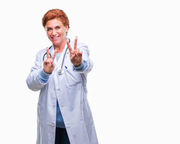 勝利のサインをやって指を表示するカメラを笑みを浮かべて隔離された背景に医療制服を着て先輩の白人医師女性 — ストック写真