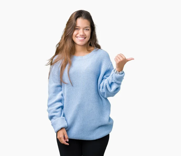 探していると親指側に上向きの幸せそうな顔を浮かべて孤立の背景に青い冬セーターを着ている若い美しいブルネットの女性 — ストック写真