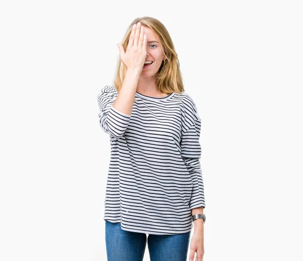 El yüz ve sürpriz duygu kendinden emin gülümseme ile tek gözüyle kapsayan izole arka plan üzerinde çizgili süveter giyen güzel genç kadın.