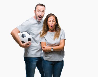 Orta yaş İspanyol çift futbol futbol topu izole arka plan üzerinde bir sürpriz yüz, korkuyor ve heyecanlı korku ifadesi ile şok korkmuş holding